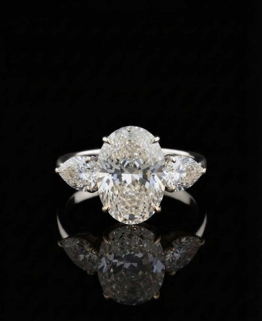 Close-up of a 5ct oval lab-grown diamond three-stone ring with pear accents in 18k white gold on a reflective black background.