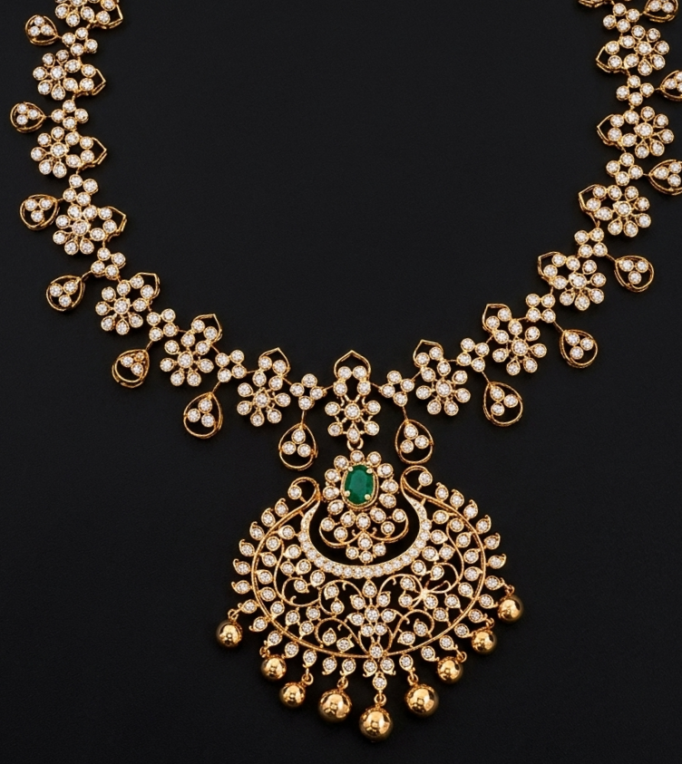 A detailed South Indian gold haram necklace displayed on a dark background. The strand consists of intricate floral stone clusters interspersed with dangling pear-shaped stone charms. At the center is a large, ornate crescent-shaped (Chandbali) pendant centered around an oval green emerald, finished with a cascading fringe of small, polished gold beads.