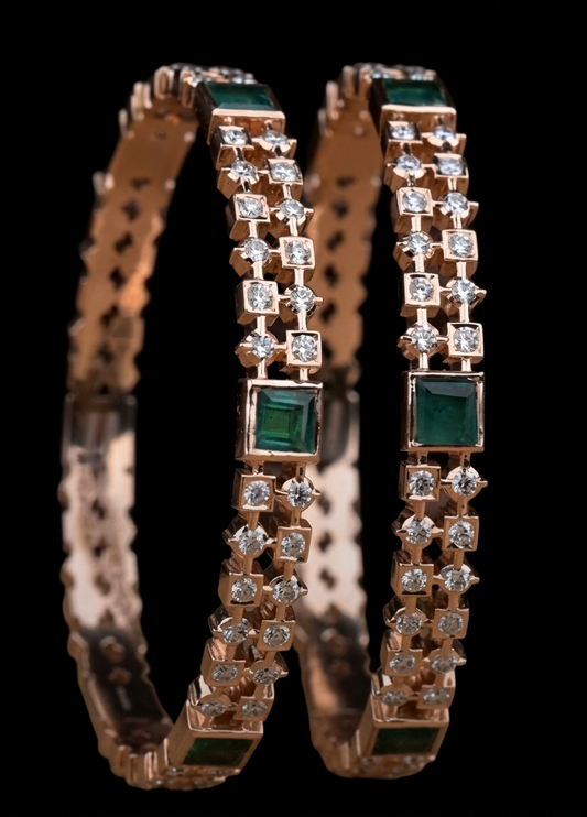 A pair of luxurious gold traditional South Indian kataka bangles set against a black background. Each bangle is intricately detailed with a central square-cut emerald (maragatham) and bordered by alternating rows of brilliant round-cut diamonds in square settings, creating a geometric checkerboard pattern. The internal band features a detailed filigree pattern.