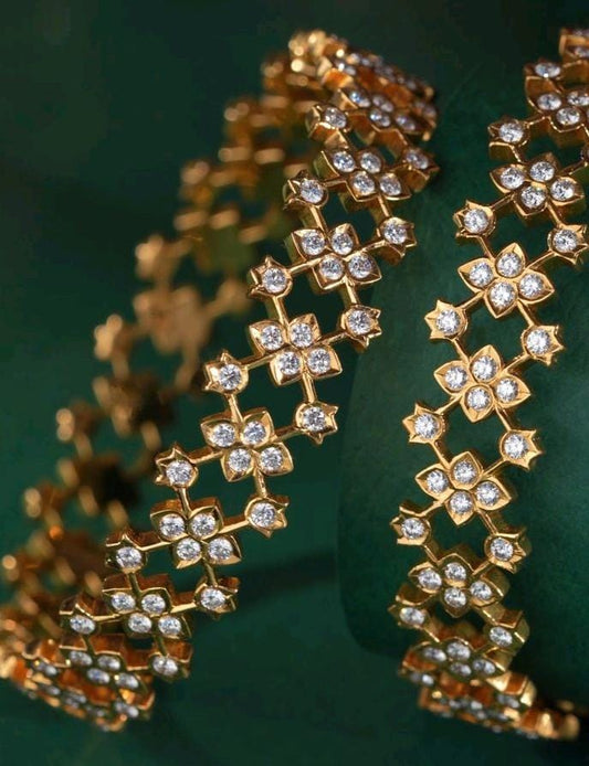 Pair of traditional South Indian gold bangles featuring intricate lattice-work diamond floral motifs set in four-petal star frames against a rich dark green backdrop