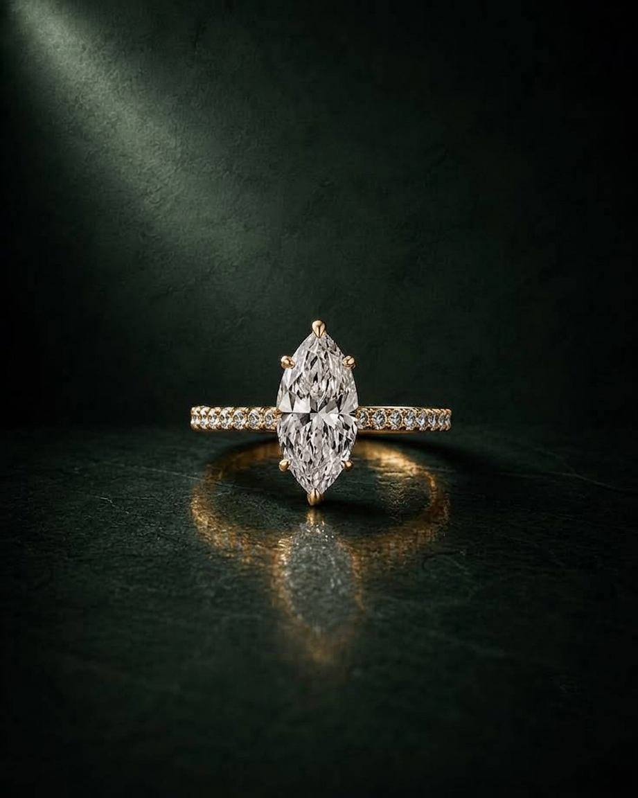 A yellow gold ring featuring a marquise-cut diamond center stone and a pavé band with small round diamonds, set against a dark textured background with dramatic lighting.