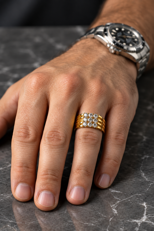 A close-up of a man's hand wearing a gold ring with a grid of small clear stones, resting on a gray marble surface. A silver-toned watch is visible on his wrist.