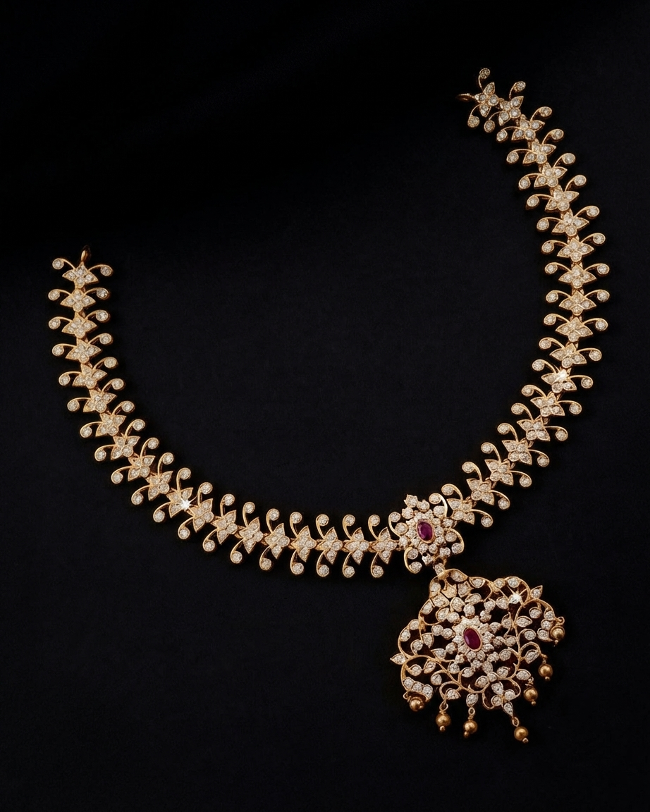 An ornate gold-toned necklace with a large pendant, embellished with clear stones and a central red gemstone, displayed on a solid black background.