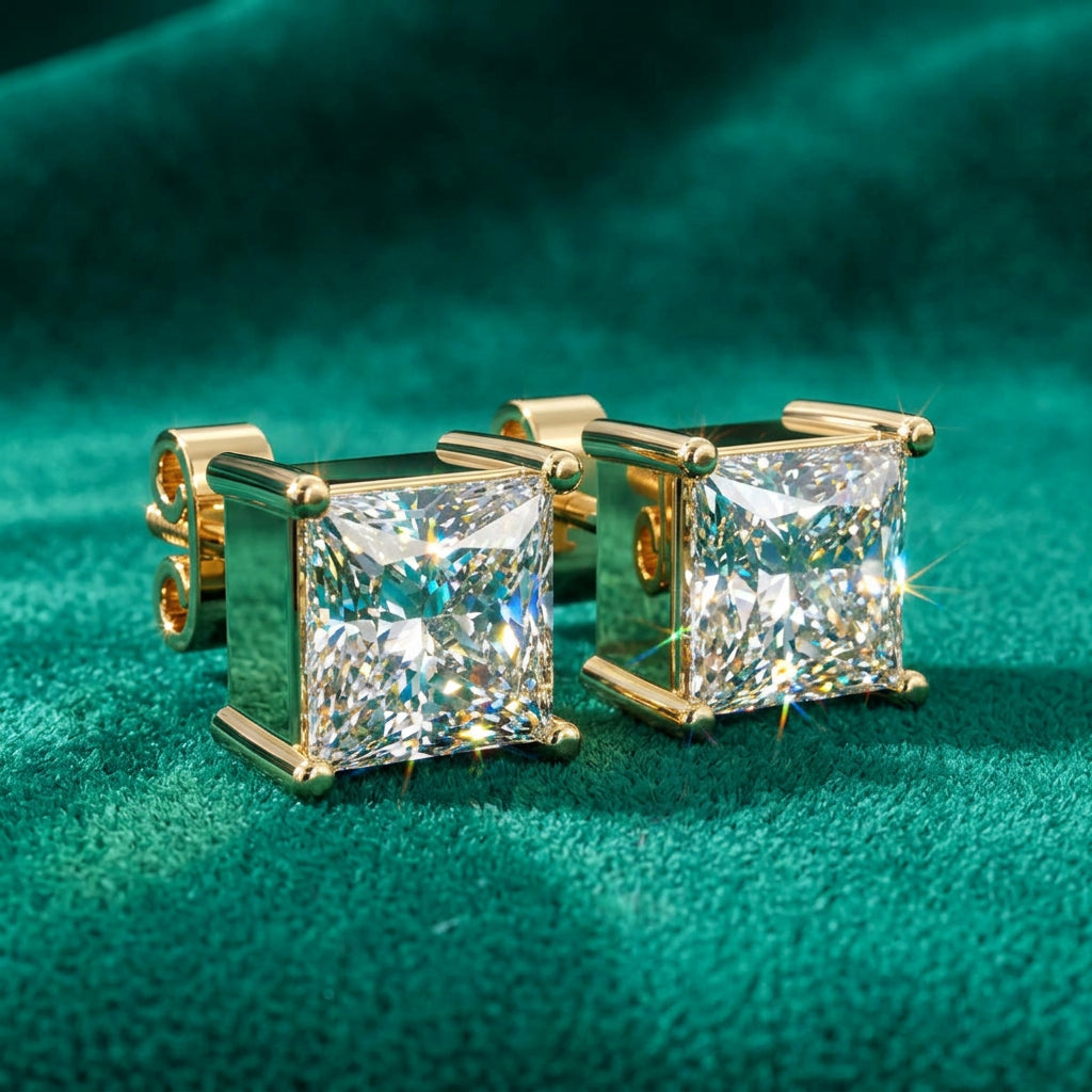 A pair of gold stud earrings with princess-cut clear diamonds, displayed on a textured dark green velvet background.