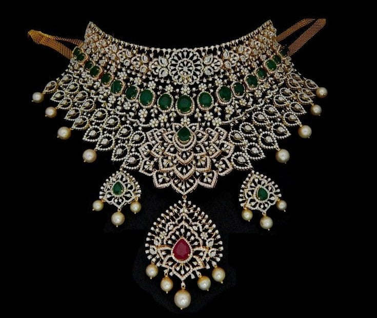 Heavy Indian bridal diamond choker set studded with oval green emeralds, pear-shaped ruby centerpiece, hanging pearl beads, and matching chandelier earrings.