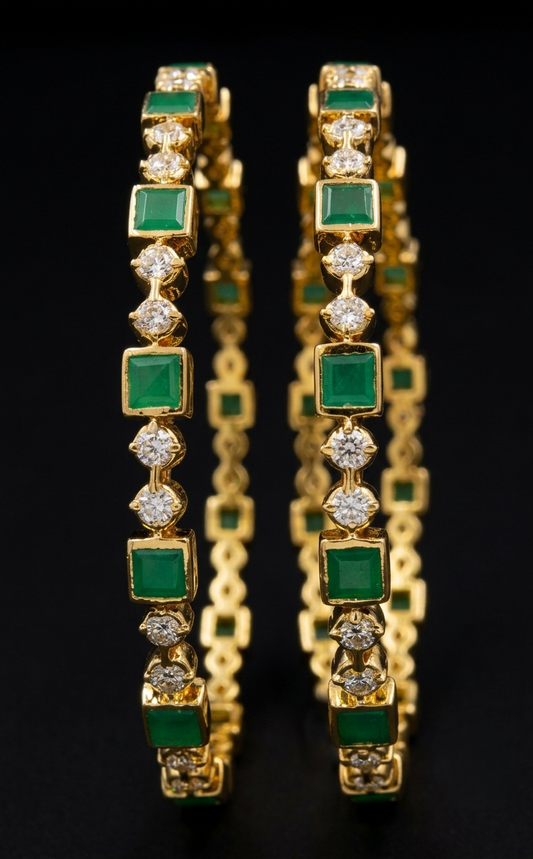 A close-up photograph of a pair of traditional South Indian 22k gold bangles set against a solid black background. The bangles feature intricate, alternating emerald (Maragatham) and diamond kempu stone clusters, each forming a geometric link pattern. The gold settings are rich and detailed, with a soft reflection of the jewelry visible on the dark surface below.