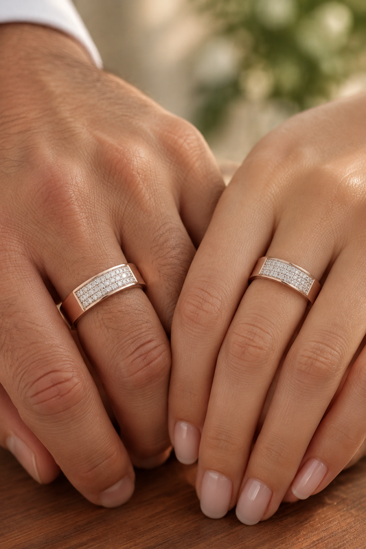 A close-up of a hand wearing a rose gold ring with a textured, pave-set silver band, resting on a dark wooden table.