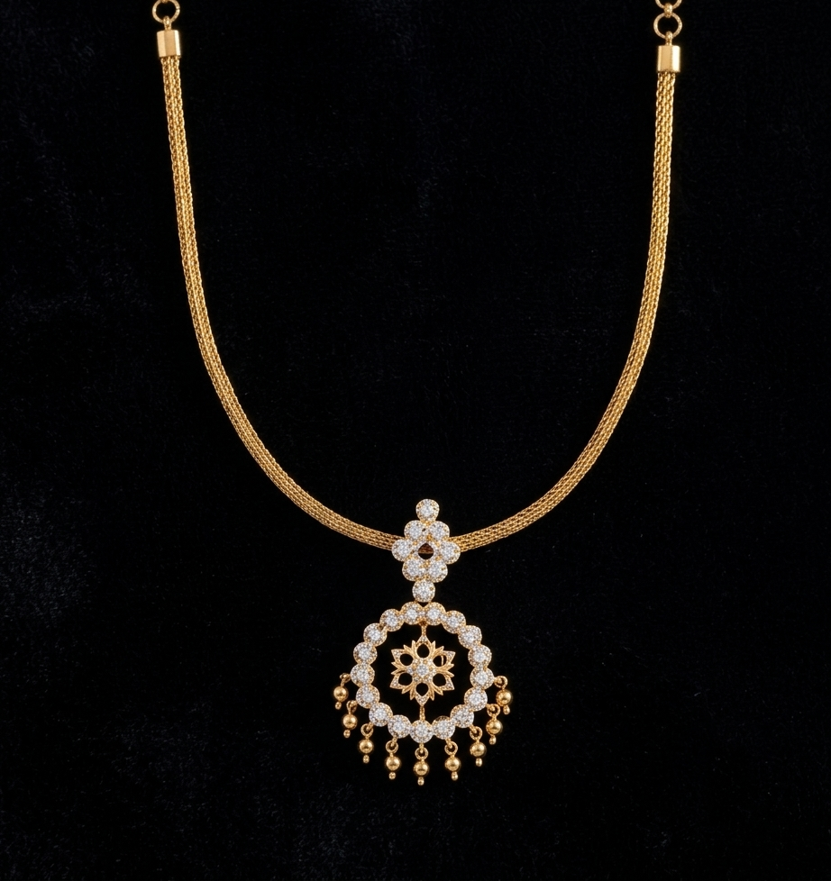 A South Indian gold necklace displayed on a dark background. The design features a smooth, flexible woven mesh gold chain supporting a diamond-shaped stone bale connected to a circular halo pendant. The pendant has an openwork center with a delicate gold floral motif, framed by sparkling clear stones and finished with a row of tiny hanging gold bead drops along the bottom rim