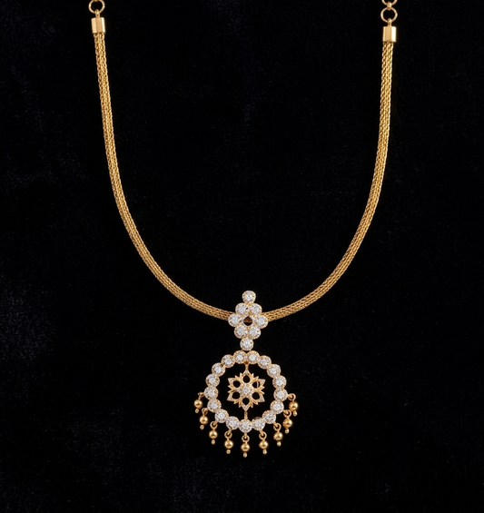 A South Indian gold necklace displayed on a dark background. The design features a smooth, flexible woven mesh gold chain supporting a diamond-shaped stone bale connected to a circular halo pendant. The pendant has an openwork center with a delicate gold floral motif, framed by sparkling clear stones and finished with a row of tiny hanging gold bead drops along the bottom rim