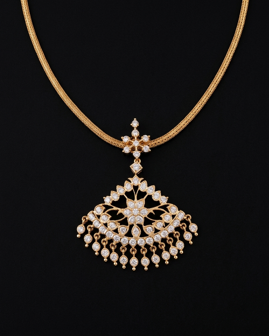 A South Indian gold necklace displayed on a dark background. The design features a smooth, thick woven gold chain supporting a star-shaped bale connected to a wide, semicircular fan pendant. The pendant is filled with intricate filigree, central flower motifs, and clear stones, finished with a cascading fringe of small round dangling stone drops.